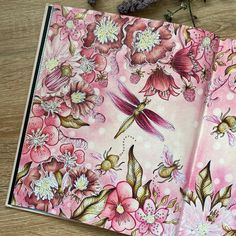 an open pink notebook with flowers and dragonflies on the cover, sitting on a wooden table