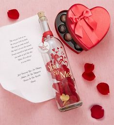 a message in a bottle next to a heart - shaped box and rose petals on a pink surface