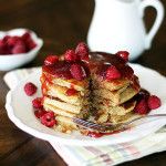 a stack of pancakes topped with raspberries on a plate next to a fork