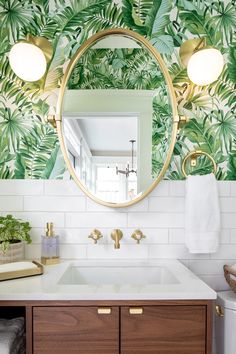 a bathroom with a mirror, sink and wallpaper in the background that has palm leaves on it