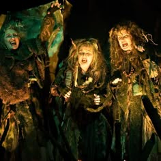 three women dressed in costumes with horns and hair are standing next to each other on stage