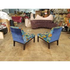 two blue chairs sitting next to each other in a room filled with couches and pillows