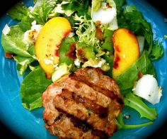 a blue plate topped with salad and meat on top of lettuce covered in peaches