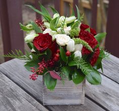 a bouquet of red and white flowers sitting on top of a wooden table with greenery