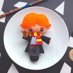 a small doll sitting on top of a white plate next to an orange and black tie