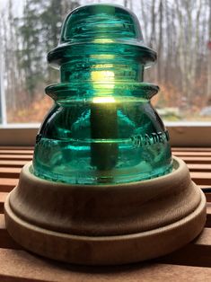 a green glass jar sitting on top of a wooden stand next to a window sill