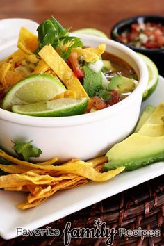 a white bowl filled with food on top of a plate next to tortilla chips