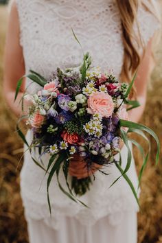 a woman holding a bouquet of flowers in her hands and wearing a white wedding dress