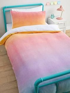 a bed with a pink and blue ombreed comforter on top of it