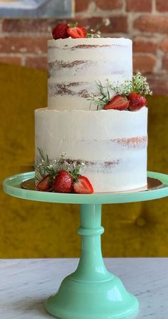 a three layer white cake with strawberries on top sitting on a green plate in front of a brick wall