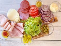 an assortment of meats, vegetables and sauces on a cutting board next to wine glasses