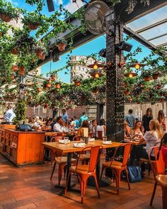 people are sitting at tables in an outdoor dining area with plants growing on the roof