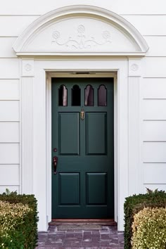 a green front door on a white house with brick walkway and boxwood trimmed hedges