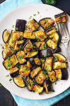 a white plate topped with cooked eggplant and parsley next to a fork