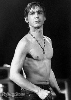 a shirtless man standing on stage with his hands in his pockets and looking off to the side