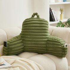 a green pillow sitting on top of a white couch next to a cup and book