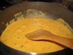 a wooden spoon in a pot filled with yellow liquid and cheese sauce on the stove