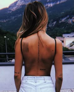 a woman with tattoos on her back standing in front of mountains