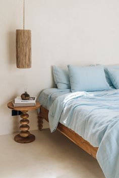 a bed with blue sheets and pillows in a white room next to a wooden table