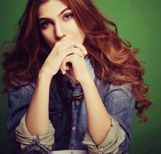 a woman with her hands on her chin and looking at the camera while wearing a denim shirt