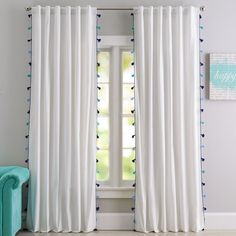 a white curtain with blue polka dots hanging in front of a window next to a chair