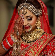 a woman in a red and gold bridal outfit holding her hands to her face