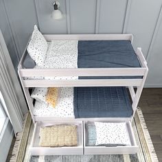 a white bunk bed with blue sheets and pillows on it's bottom shelf next to a window