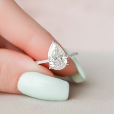 a woman's hand holding an engagement ring with a pear shaped diamond on it