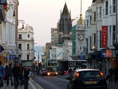 people are walking down the street in front of some buildings and cars on the road