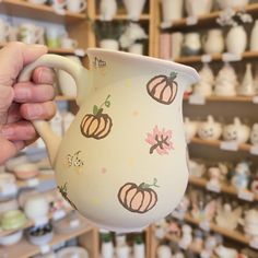 a hand holding a coffee mug with pumpkins on it in front of many other items