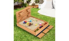 an open wooden sandbox with toys in it on the grass next to some stairs