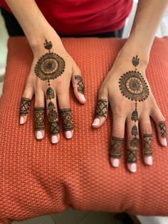 a woman's hands with henna tattoos on her fingers and hand, sitting on an orange cushion