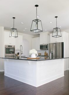 a kitchen with white cabinets and stainless steel appliances, including an island in the middle