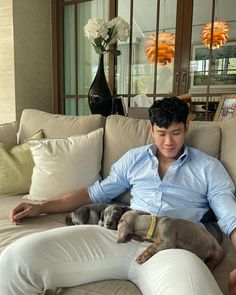 a man sitting on a couch with two dogs in his lap and one is holding the other