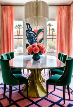 a dining room table with green chairs and pink curtains in front of a window that has palm trees on it