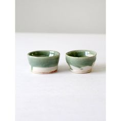 two small green and white bowls sitting on top of a white countertop next to each other