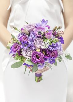 a bride holding a purple bouquet in her hands