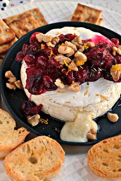 a black plate topped with cheese covered in cranberry sauce next to crackers