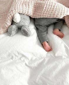 a baby laying in bed under a blanket with a stuffed animal on it's side