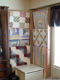 a room with many quilts on the wall and a chair in front of it