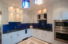 a kitchen with white cabinets and blue backsplashes on the counters, lights above