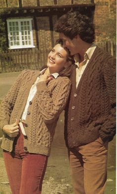 two people standing next to each other in front of a brick building and one person is wearing a sweater