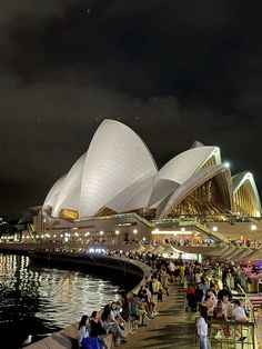 people are sitting at tables in front of the sydney opera house, lit up at night