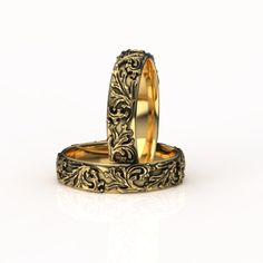 two gold wedding rings sitting on top of each other, with floral designs in the middle