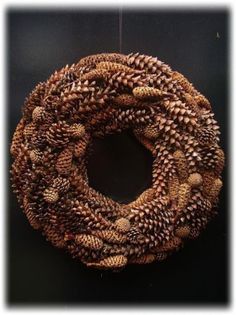 a wreath made out of pine cones hanging on a door hanger in front of a black wall