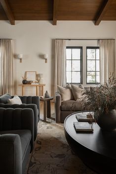 a living room with couches, tables and two windows in the wall behind them