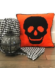 an orange pillow with a skull on it next to a black and white checkered blanket