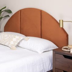 a bed with white sheets and pillows next to a brown headboard on a wooden night stand