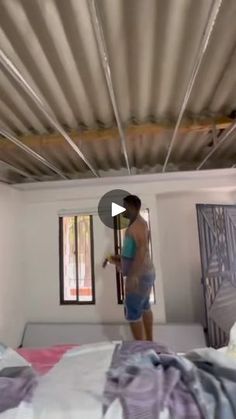 a man standing on top of a bed in a room with white walls and metal beams