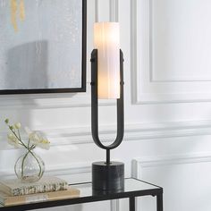 a black table lamp with a white candle on it in front of a framed mirror